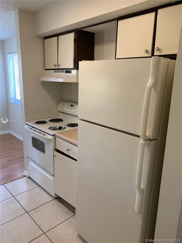 kitchen with white cabinets, white appliances, a textured ceiling, and light tile patterned floors