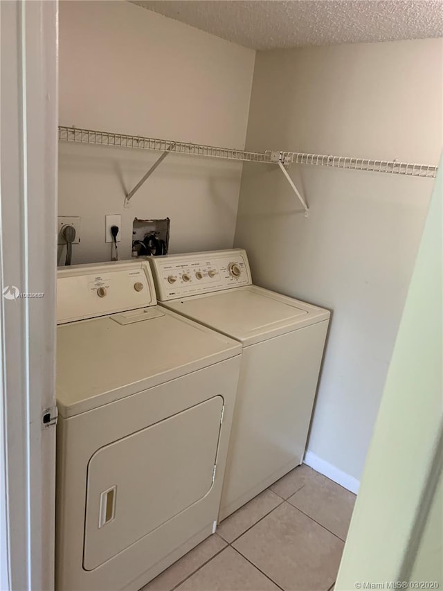 clothes washing area with light tile patterned floors, a textured ceiling, and washing machine and clothes dryer