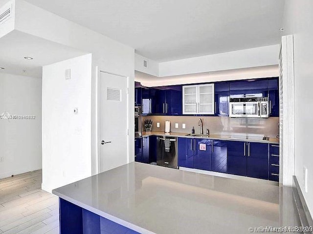 kitchen with modern cabinets, stainless steel appliances, light wood-type flooring, blue cabinetry, and a sink