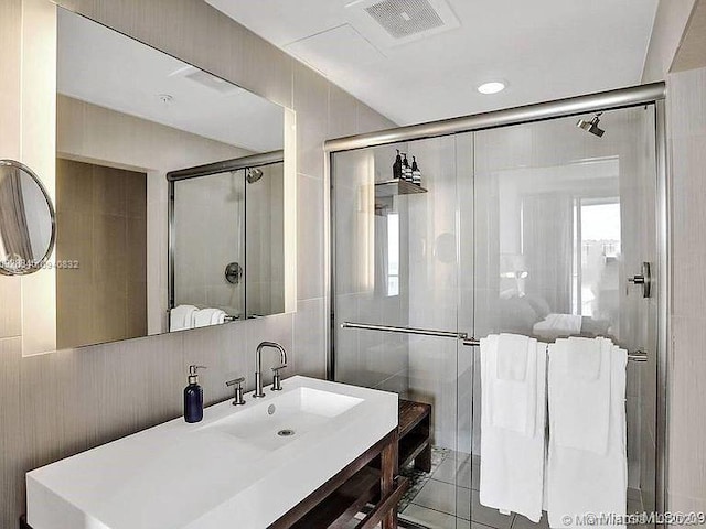 bathroom with a shower with shower door, vanity, and tile walls