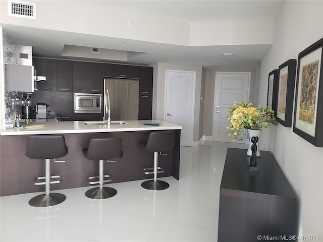 kitchen featuring light tile floors, stainless steel microwave, fridge, and a breakfast bar