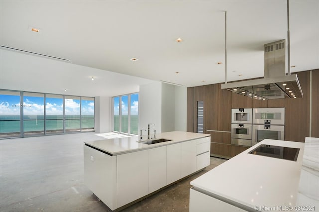 kitchen with concrete flooring, white cabinetry, ventilation hood, and a kitchen island with sink