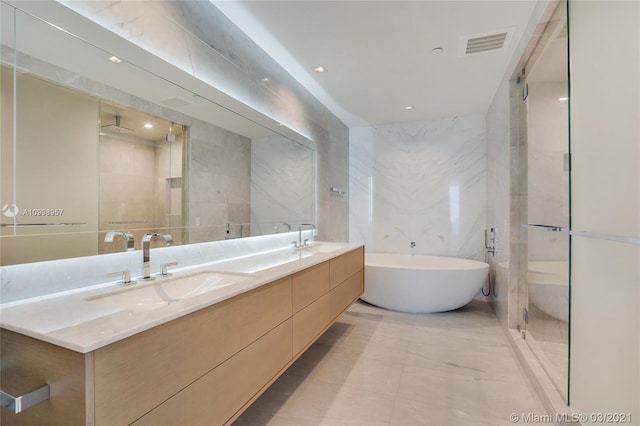 bathroom with tile walls, double sink, plus walk in shower, tile floors, and oversized vanity