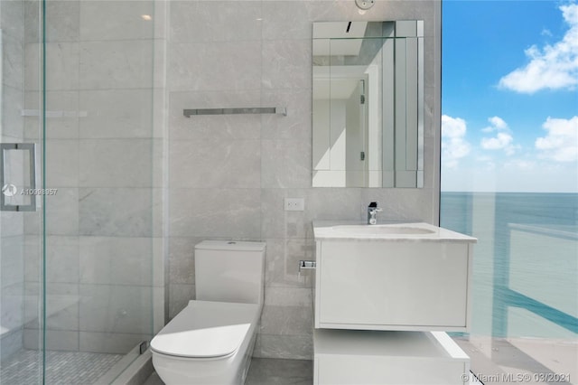 bathroom featuring tile walls, toilet, a shower with shower door, a water view, and vanity