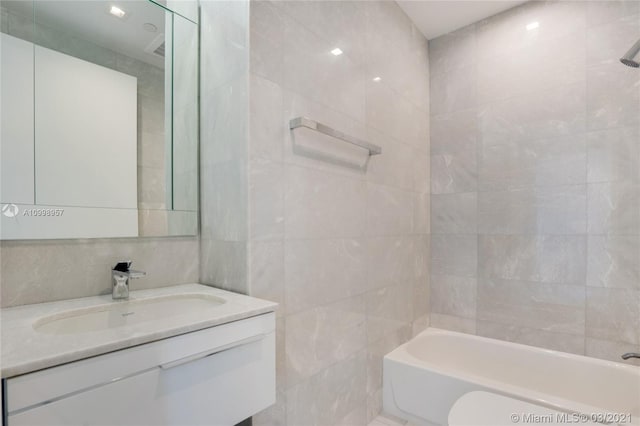 full bathroom with tile walls, toilet, vanity, and tiled shower / bath