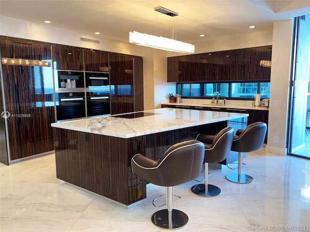 kitchen with light stone counters, hanging light fixtures, a breakfast bar area, and a center island