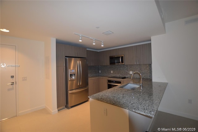 kitchen with stainless steel appliances, kitchen peninsula, backsplash, stone counters, and sink