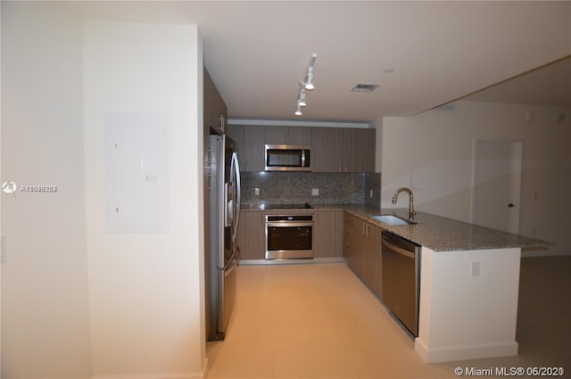 kitchen featuring dark stone counters, kitchen peninsula, rail lighting, appliances with stainless steel finishes, and sink