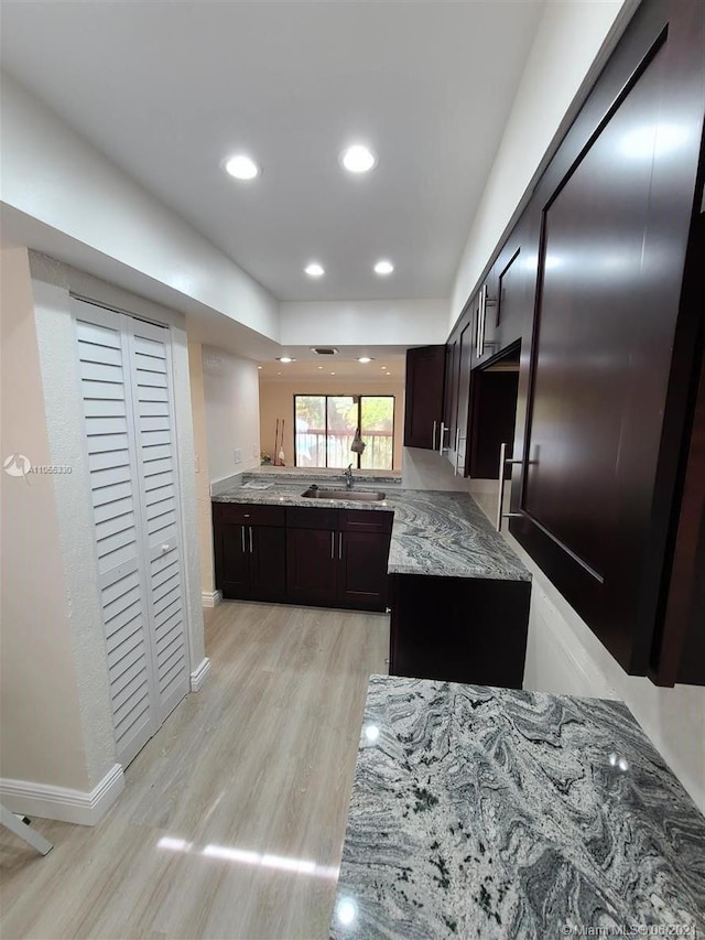 kitchen with light stone countertops, dark brown cabinets, light hardwood / wood-style flooring, and sink