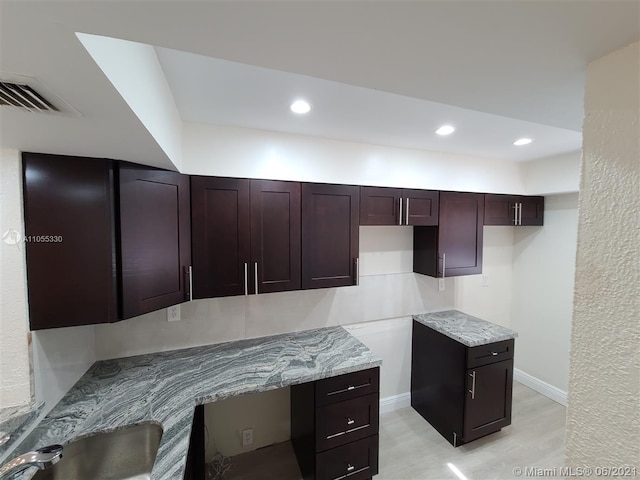 kitchen with dark brown cabinetry, sink, light stone counters, light hardwood / wood-style flooring, and built in desk