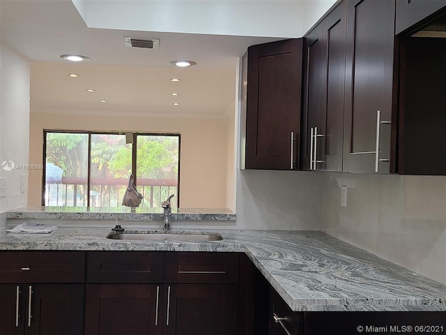 kitchen with dark brown cabinetry, crown molding, sink, and light stone counters