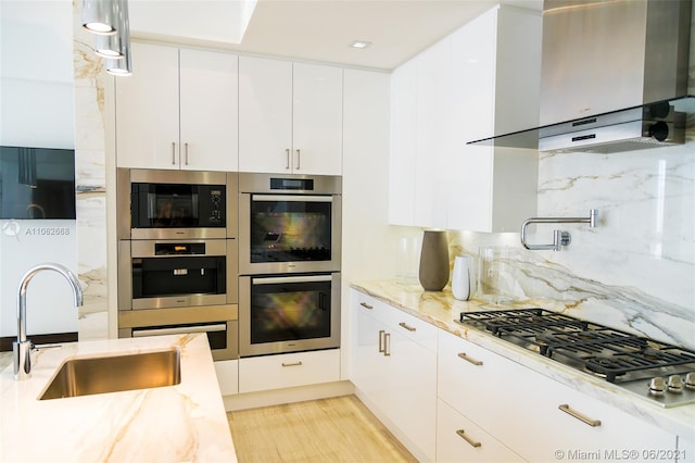 kitchen with light stone counters, sink, white cabinetry, wall chimney exhaust hood, and appliances with stainless steel finishes