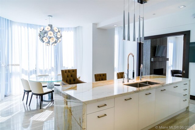 kitchen with pendant lighting, light stone counters, sink, an island with sink, and white cabinetry