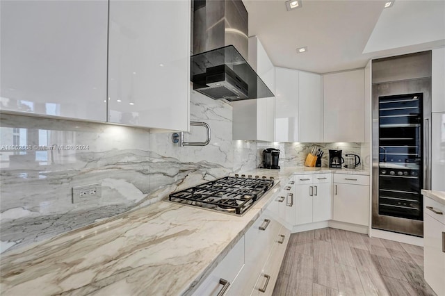 kitchen featuring light hardwood / wood-style floors, white cabinetry, wall chimney exhaust hood, light stone countertops, and stainless steel gas stovetop