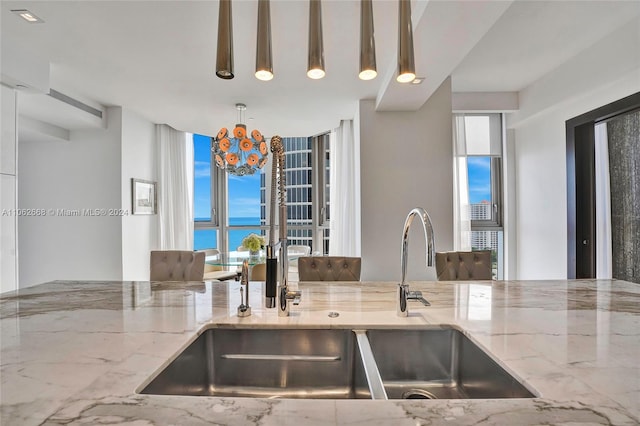 kitchen with an inviting chandelier, hanging light fixtures, light stone countertops, and sink