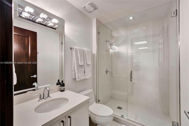 bathroom featuring a shower with door, vanity, and toilet