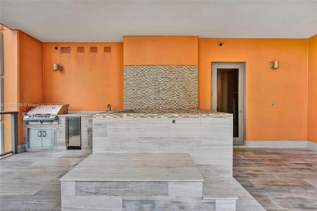 kitchen with stainless steel refrigerator, kitchen peninsula, backsplash, and light stone countertops