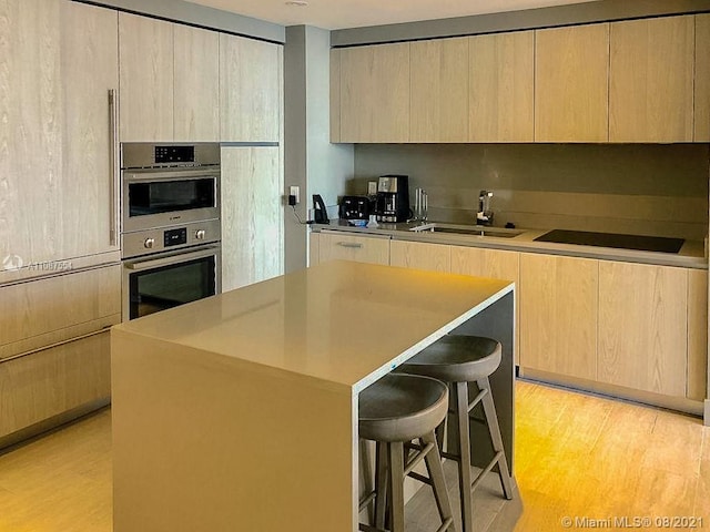 kitchen featuring double oven, a kitchen breakfast bar, sink, light hardwood / wood-style flooring, and a kitchen island