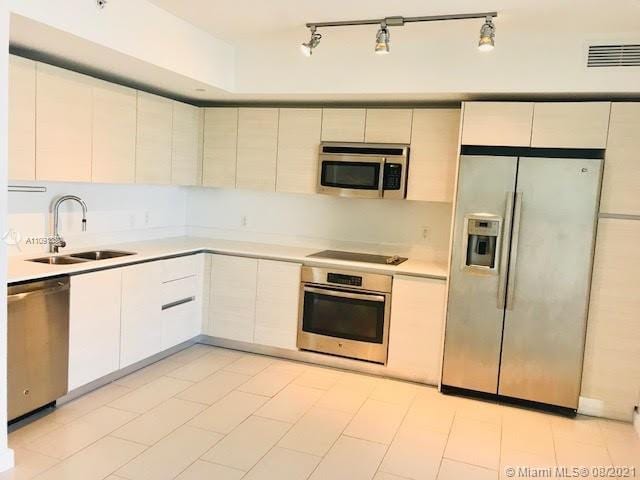 kitchen featuring white cabinetry, light tile flooring, appliances with stainless steel finishes, track lighting, and sink