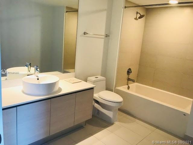 full bathroom with tiled shower / bath, toilet, tile floors, and vanity