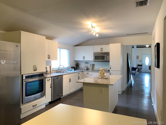 kitchen with stainless steel appliances, a center island, vaulted ceiling, white cabinets, and dark tile floors