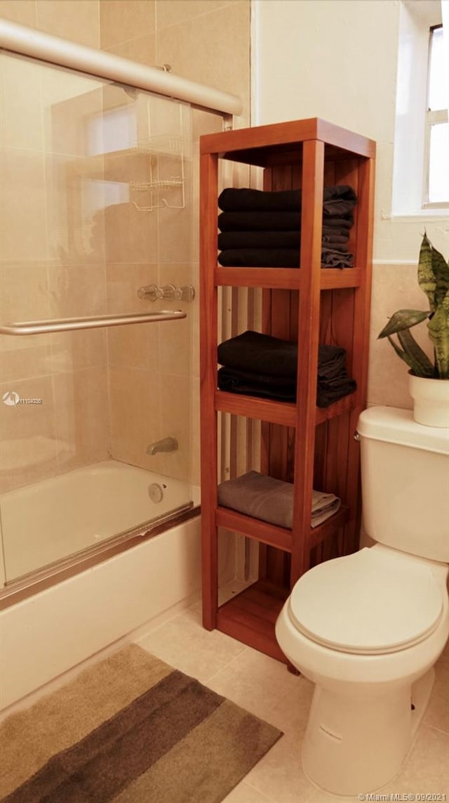 bathroom with combined bath / shower with glass door, toilet, and tile floors