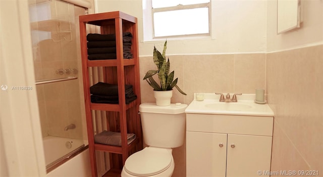 full bathroom featuring bath / shower combo with glass door, oversized vanity, toilet, and tile walls