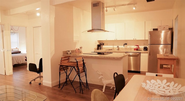 kitchen featuring stainless steel appliances, light hardwood / wood-style flooring, wall chimney exhaust hood, and white cabinetry