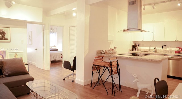 kitchen featuring light stone counters, rail lighting, stainless steel dishwasher, light hardwood / wood-style flooring, and wall chimney exhaust hood