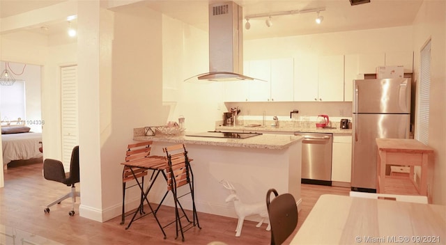 kitchen featuring white cabinets, light hardwood / wood-style flooring, a breakfast bar area, stainless steel appliances, and wall chimney range hood