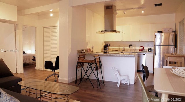 interior space with dark hardwood / wood-style floors, appliances with stainless steel finishes, white cabinets, light stone counters, and wall chimney range hood