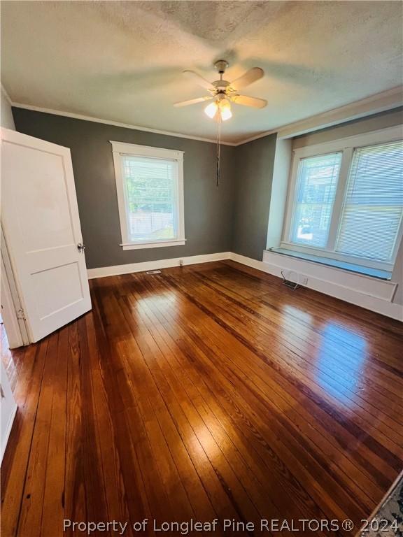 empty room featuring a textured ceiling, ceiling fan, dark hardwood / wood-style floors, and ornamental molding