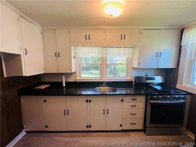 kitchen featuring stainless steel gas stove, white cabinetry, dark stone counters, and sink