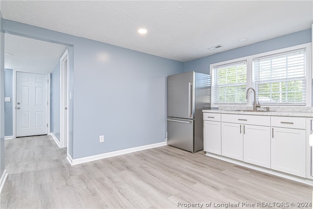 kitchen with white cabinetry, light hardwood / wood-style floors, sink, stainless steel fridge, and a textured ceiling