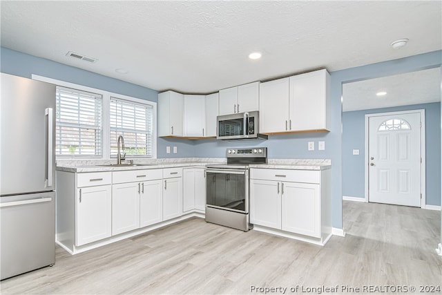 kitchen with appliances with stainless steel finishes, white cabinets, sink, light wood-type flooring, and a textured ceiling