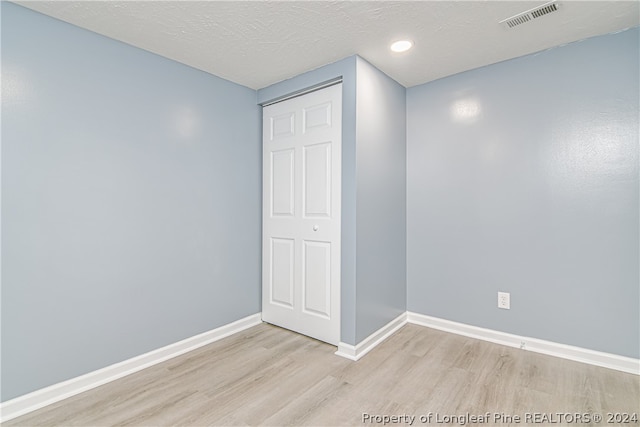 unfurnished room with a textured ceiling and light wood-type flooring