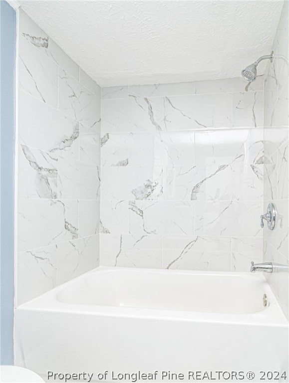 bathroom with a textured ceiling and tiled shower / bath combo