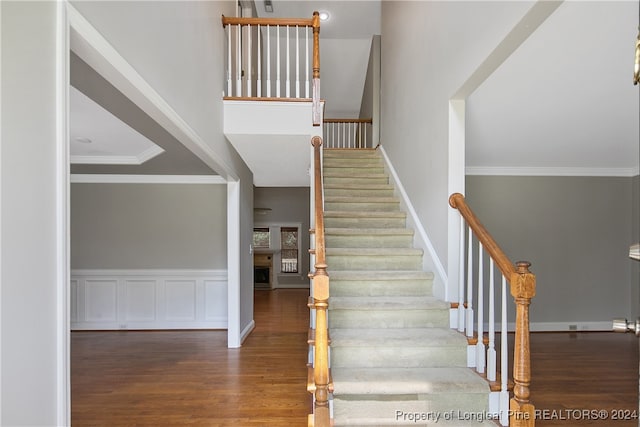 stairs featuring wood-type flooring, crown molding, and a towering ceiling