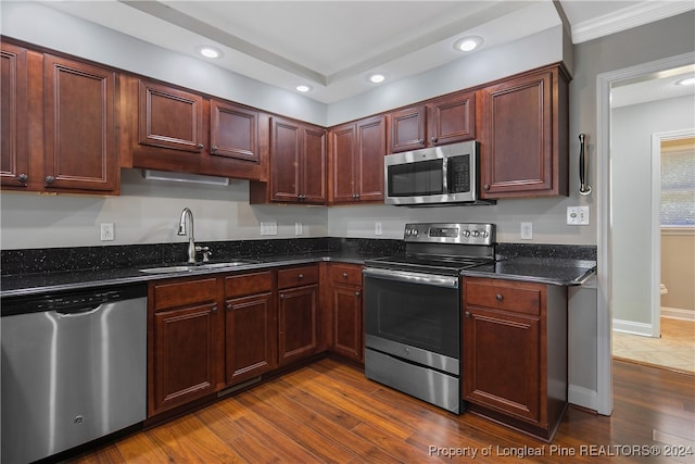 kitchen with appliances with stainless steel finishes, sink, dark stone counters, and dark hardwood / wood-style floors