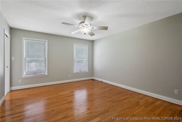 empty room with a textured ceiling, a healthy amount of sunlight, ceiling fan, and wood-type flooring