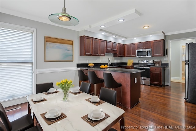 kitchen featuring hanging light fixtures, appliances with stainless steel finishes, dark wood-type flooring, a kitchen breakfast bar, and ornamental molding