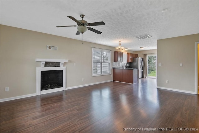 unfurnished living room with dark hardwood / wood-style flooring, ceiling fan with notable chandelier, and plenty of natural light