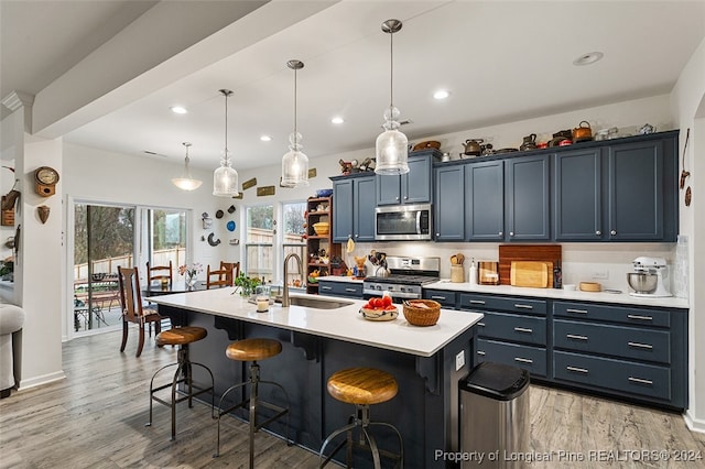 kitchen with appliances with stainless steel finishes, sink, light wood-type flooring, a kitchen island with sink, and a breakfast bar