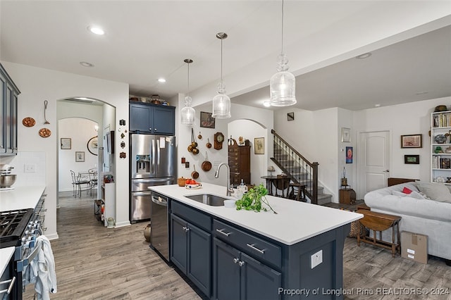 kitchen featuring sink, light wood-type flooring, appliances with stainless steel finishes, decorative backsplash, and a kitchen island with sink