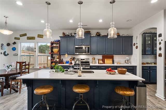 kitchen with appliances with stainless steel finishes, light hardwood / wood-style flooring, backsplash, a kitchen bar, and pendant lighting