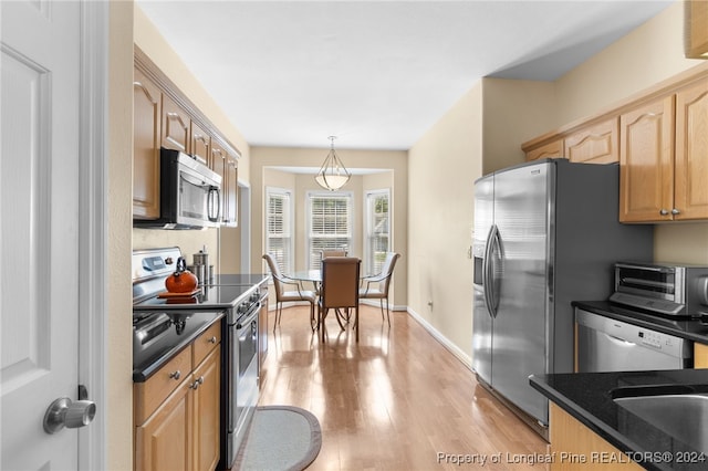 kitchen with decorative light fixtures, stainless steel appliances, sink, light wood-type flooring, and dark stone counters