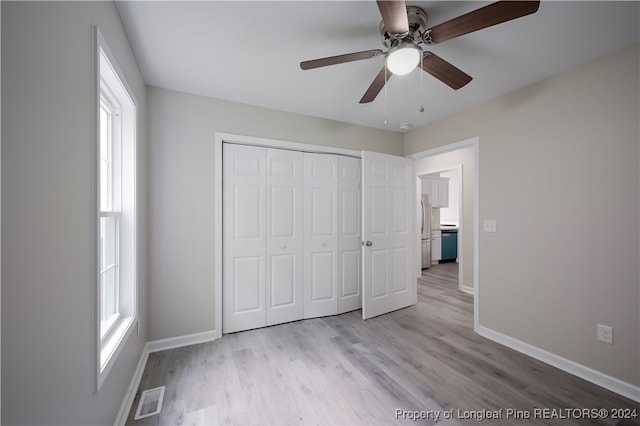 unfurnished bedroom featuring light hardwood / wood-style floors, a closet, stainless steel fridge, and ceiling fan