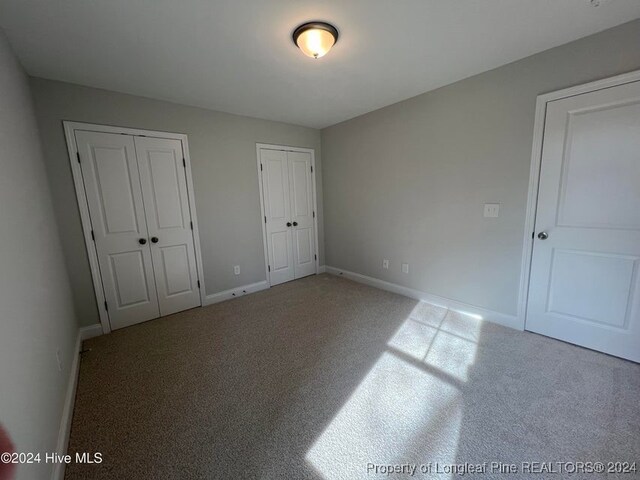 unfurnished bedroom featuring light carpet and multiple closets