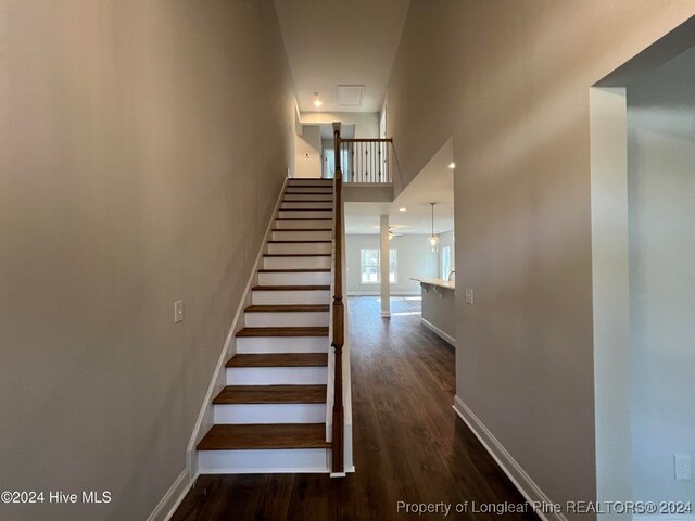 staircase with wood-type flooring, a towering ceiling, and ceiling fan