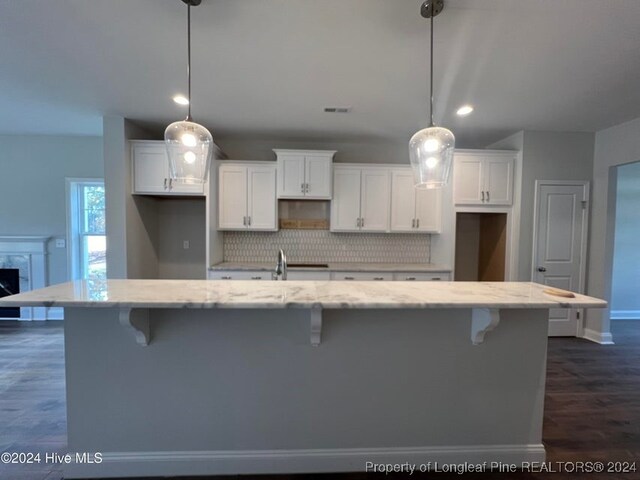 kitchen featuring pendant lighting, dark hardwood / wood-style floors, white cabinets, and a large island with sink